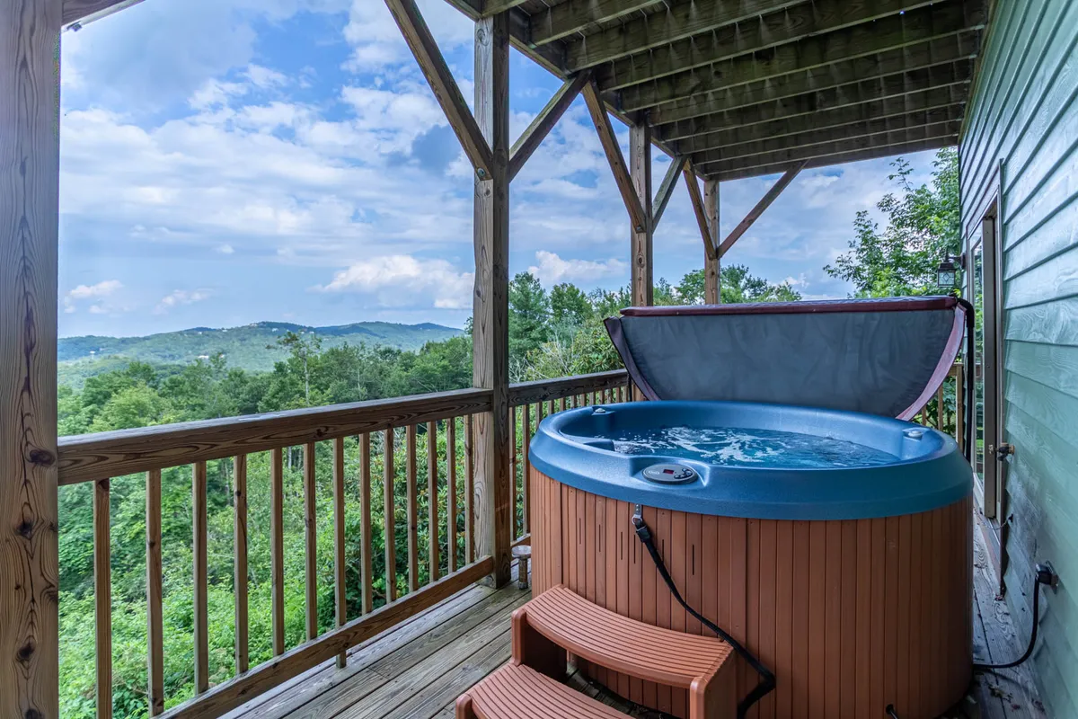 On the lower deck, the hot tub takes center stage, overlooking a tranquil mountain landscape. The wooden railing and scenic backdrop create an inviting outdoor wellness retreat, perfectly suited for relaxing, soaking, and enjoying the views any time of day.