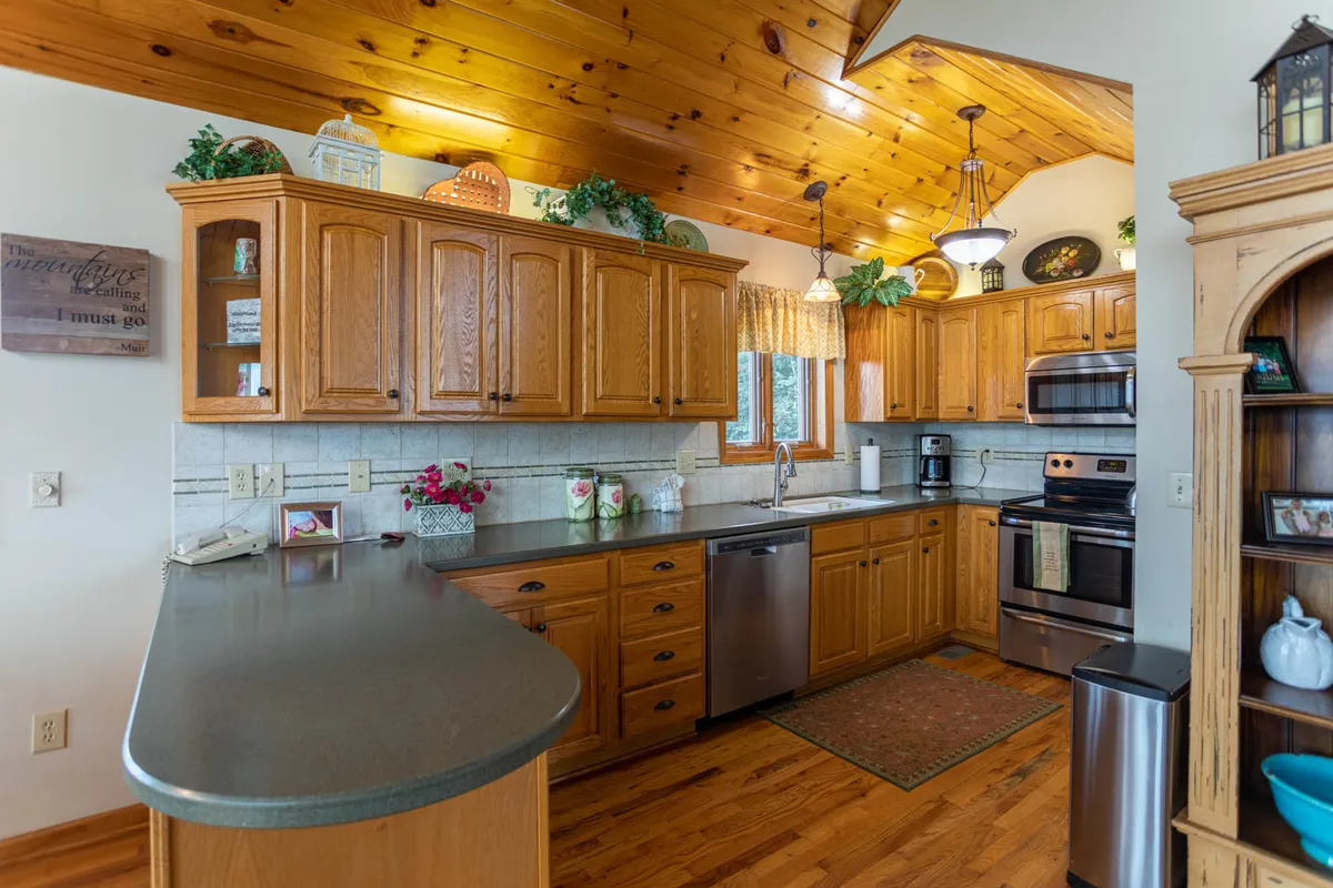A modern kitchen with wooden cabinetry, stainless steel appliances including a refrigerator and oven, decorative lighting, and a welcoming countertop space. The kitchen is clearly designed for group meal preparation and features the kind of amenities mentioned in the section.