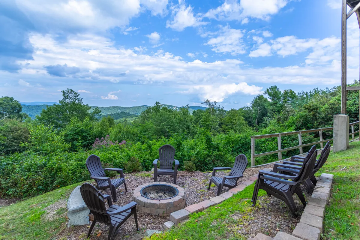 The scene features a fire pit area with Adirondack chairs set against a sweeping mountain view. The setup invites guests to socialize, share stories, or roast marshmallows in a relaxed, scenic outdoor environment.
