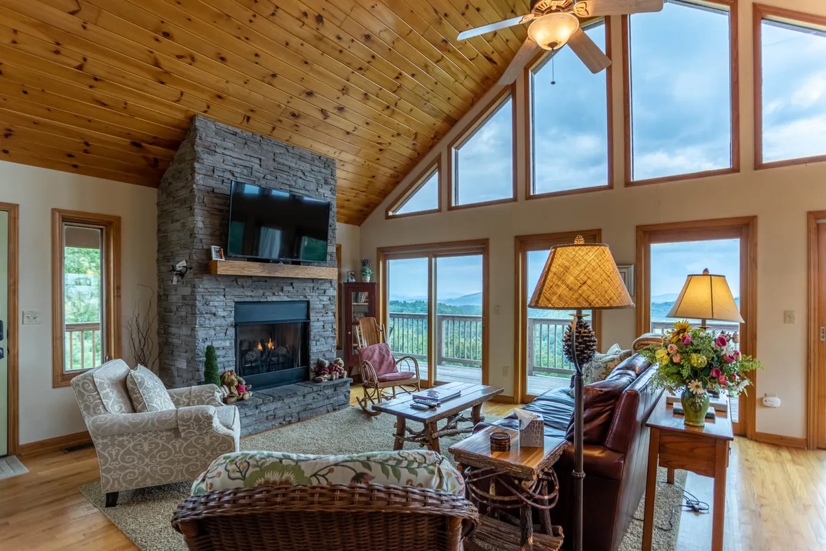 A cozy living room with a fireplace, large windows offering sunrise views, and comfortable seating arranged for relaxation. The windows provide glimpses of the outdoors, hinting at the natural surroundings and inviting atmosphere.