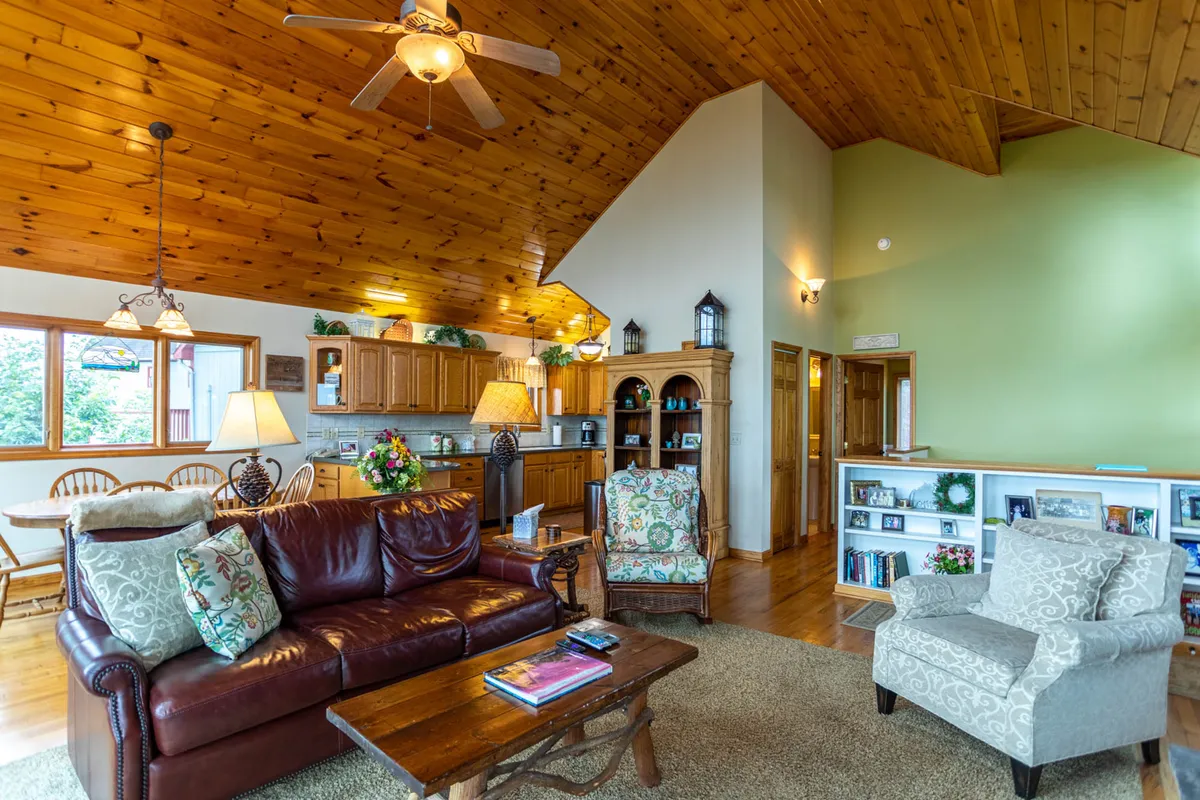 This inviting living area features a leather sofa set beneath a wooden ceiling, a dining table ready for shared meals, and a bookshelf filled with books. The space is designed for family gatherings, meal preparation, and relaxing evenings by the fireplace, evoking the warmth and comfort of a mountain retreat.
