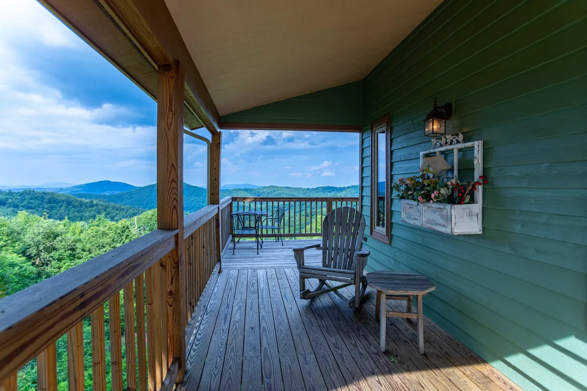 A cozy corner of the wooden deck featuring a classic Adirondack chair and small table, positioned to take in sweeping mountain views. Decorative touches like a flower box on the railing add charm, while the tranquil morning or evening light sets a peaceful mood perfect for coffee or stargazing.